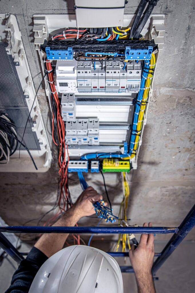Un electricista trabaja en un cuadro de distribución con un cable de conexión eléctrica