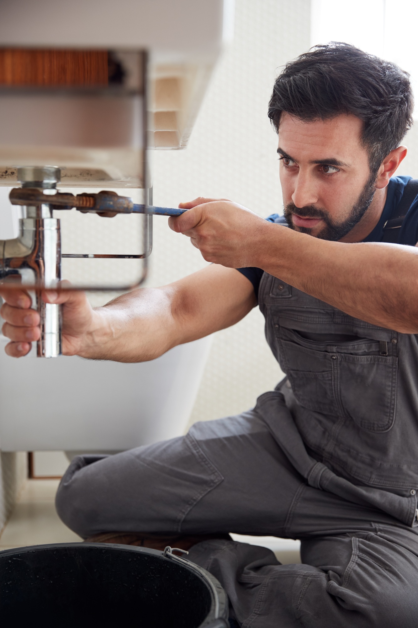 Fontanero urgente usando una llave inglesa para arreglar una fuga en el lavabo del baño